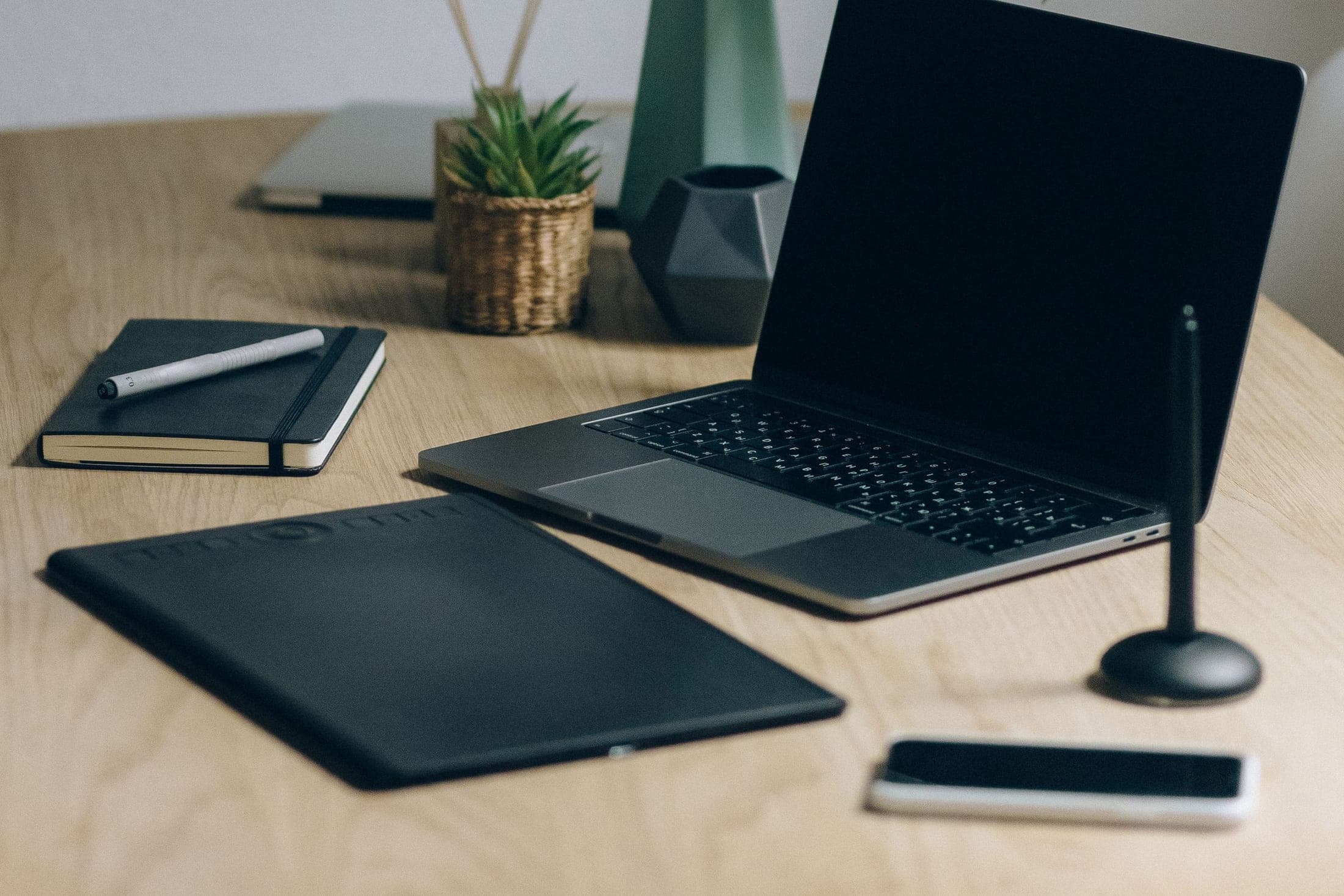 A minimalist digital workspace with a laptop, notebook, and plant